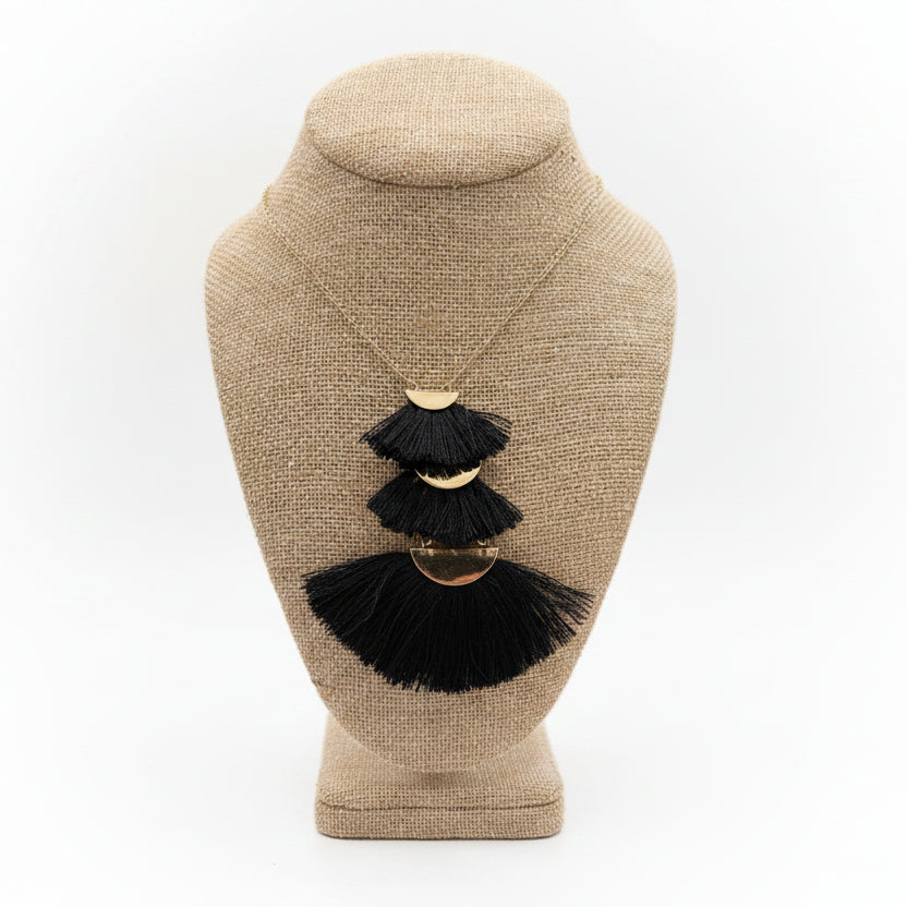 Black tassel earrings on a beige jewelry display