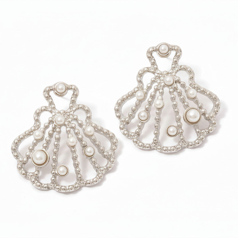 Pair of ornate shell earrings with pearls on a white surface