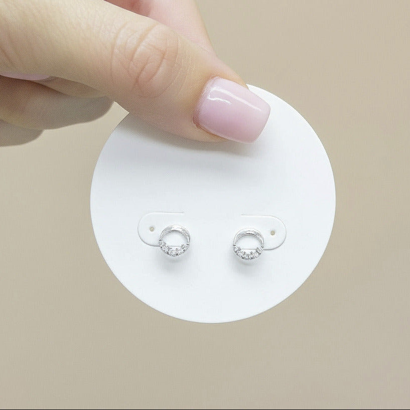 Hand holding a small round card with earrings against a neutral background
