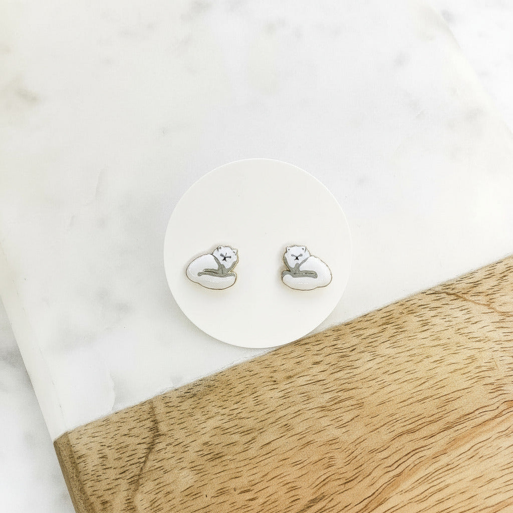 white long haired cat stud earrings placed on a marble surface.