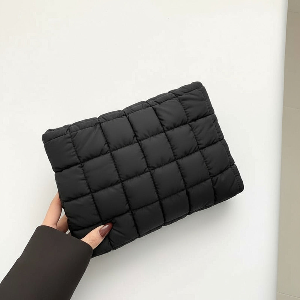 Black quilted clutch held by a hand against a neutral background
