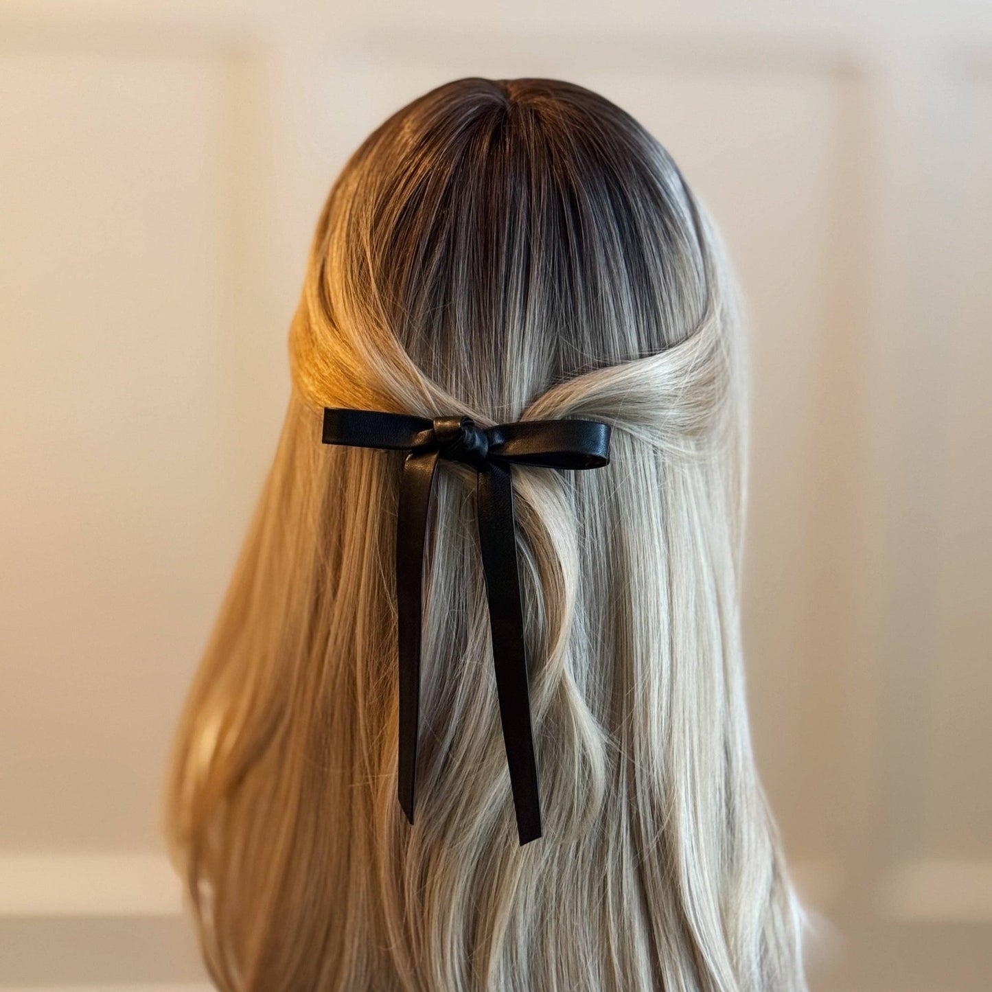 Person with long, wavy hair tied with a black hair bow against a neutral background