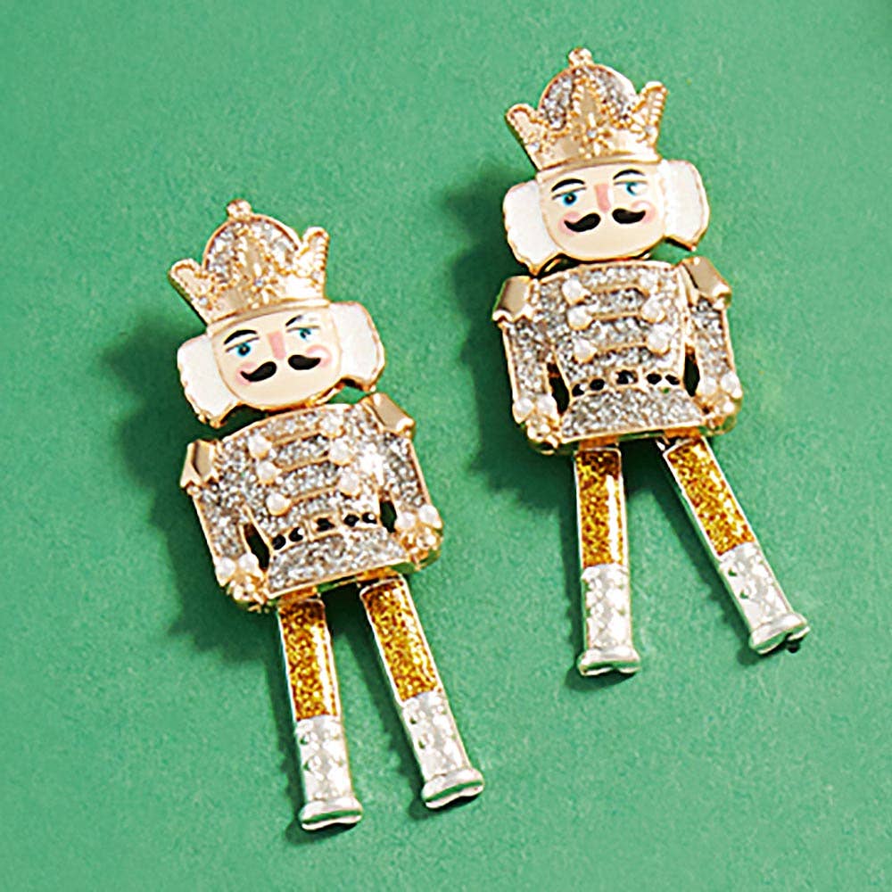 Gold and silver nutcracker-shaped earrings on a green background