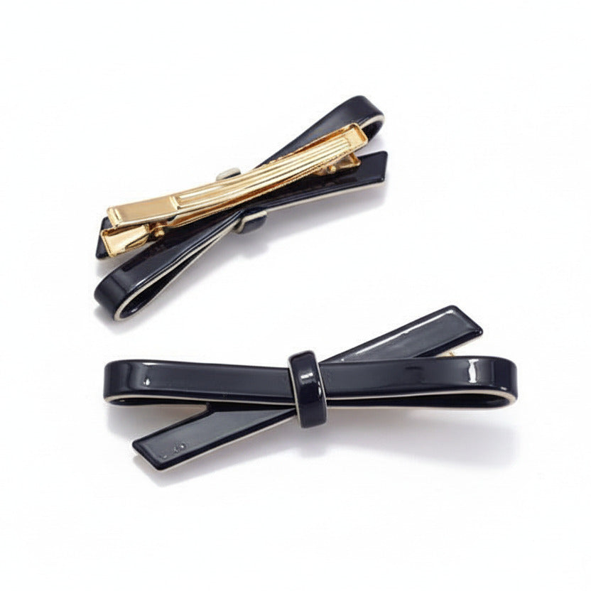 Two hair clips, with a black bow design, on a white background.