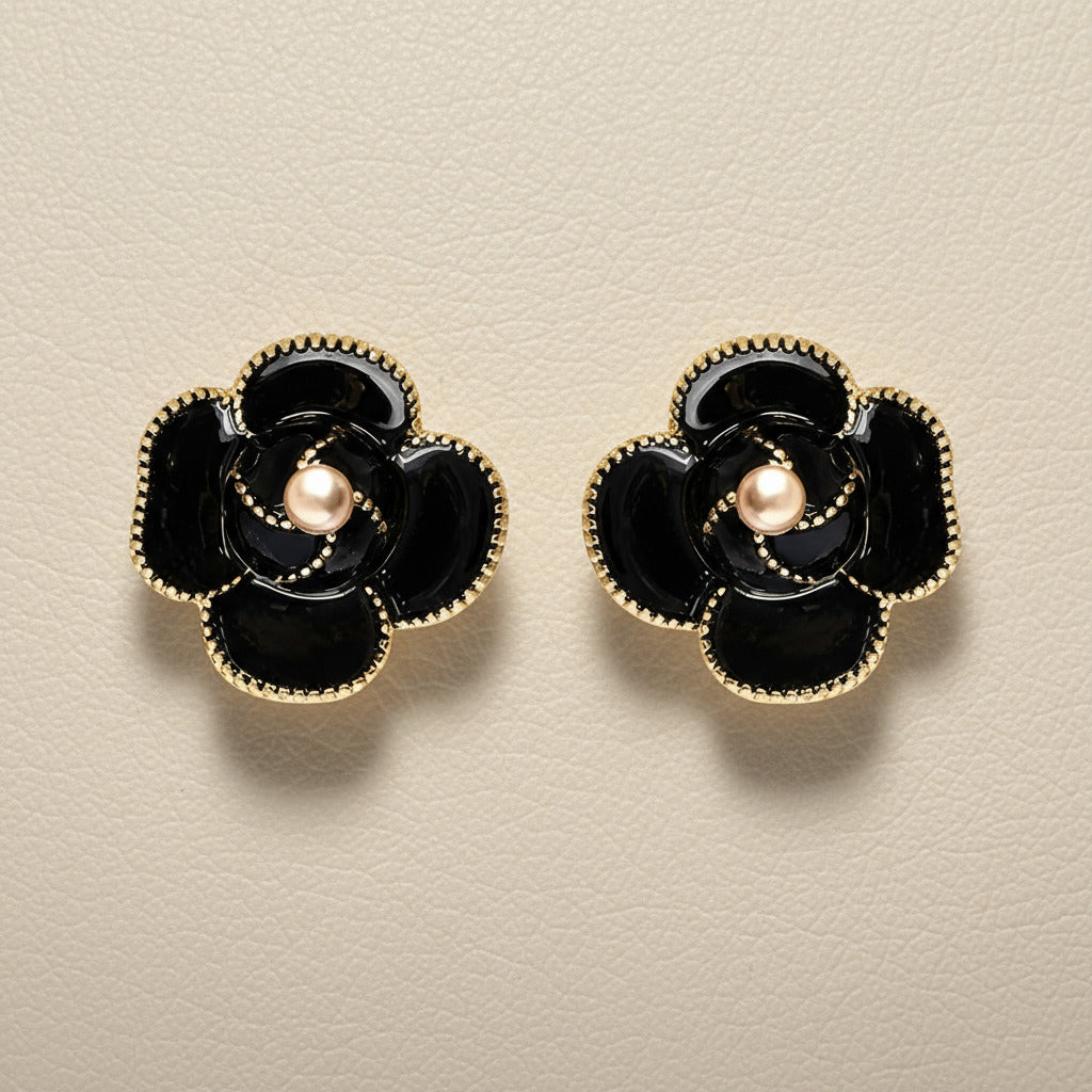 Black flower-shaped earrings with gold accents on a textured surface