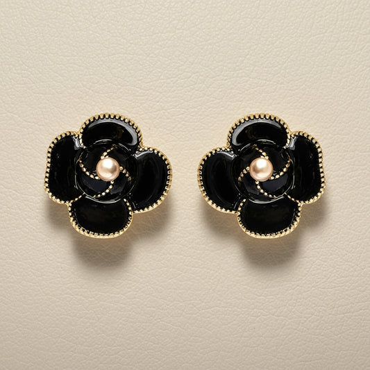Black flower-shaped earrings with gold accents on a textured surface