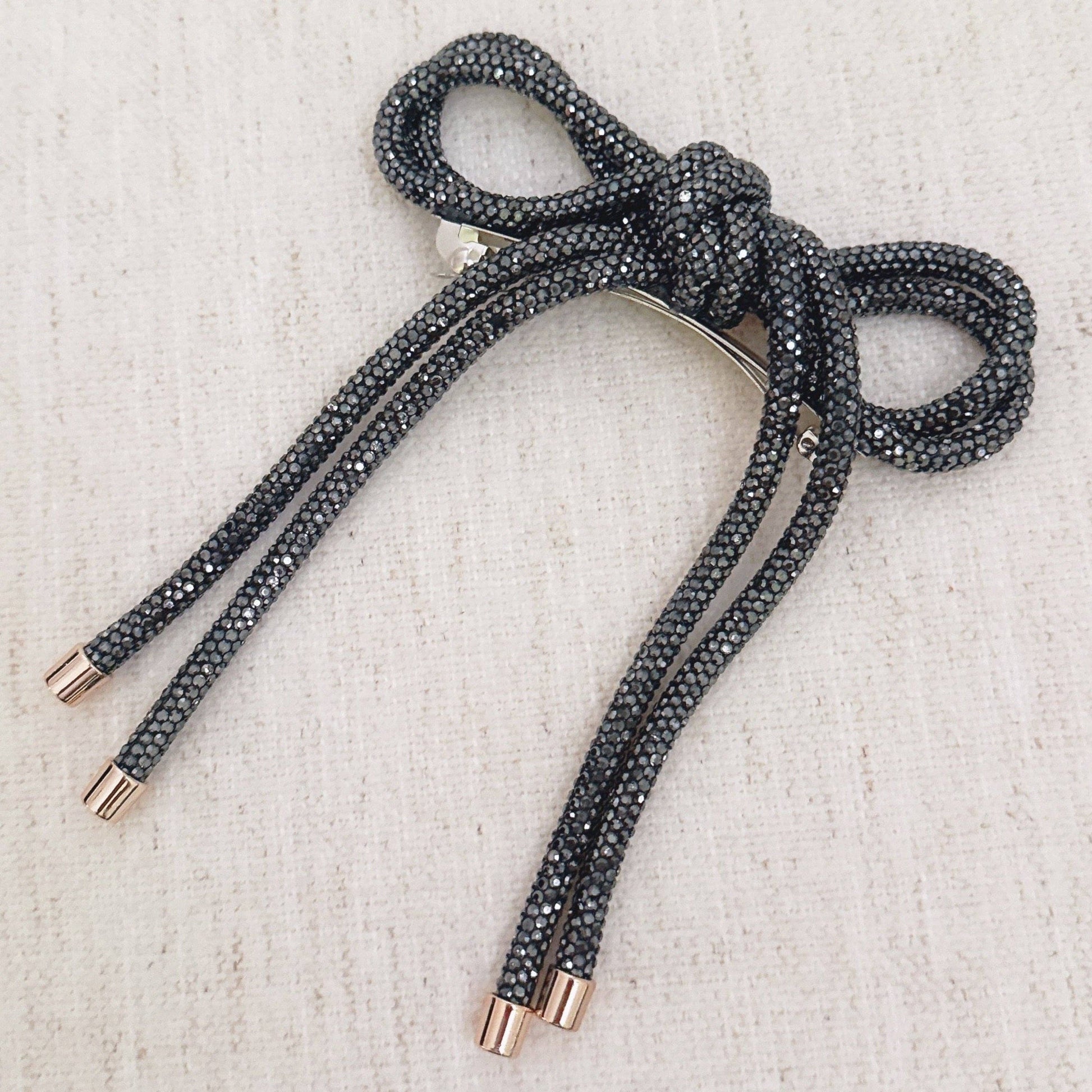 Black sparkly bow hair clip on a textured beige background