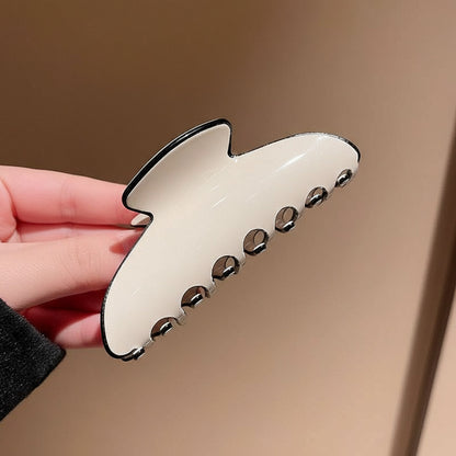 Cream hair clip with black edges held by a hand against a beige background