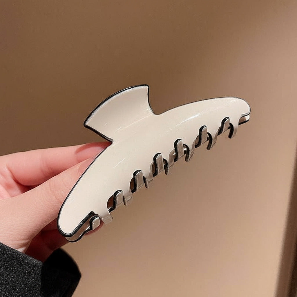 Cream hair clip with black accents held by a hand against a beige background