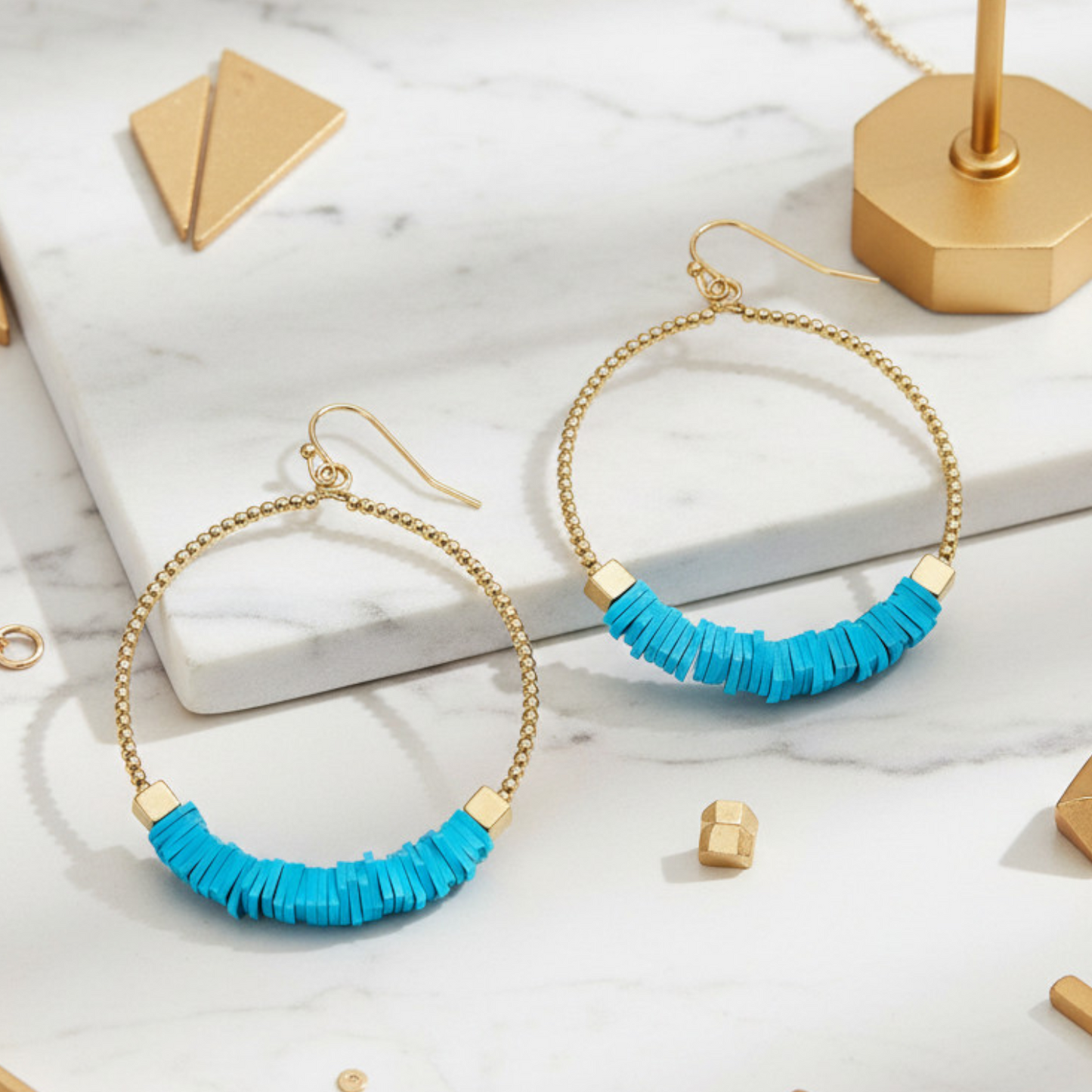 Gold hoop earrings with turquoise beads on a marble surface