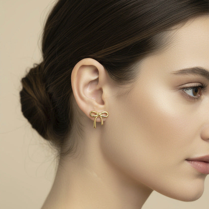 Gold bow-shaped earring worn by a model on a beige background