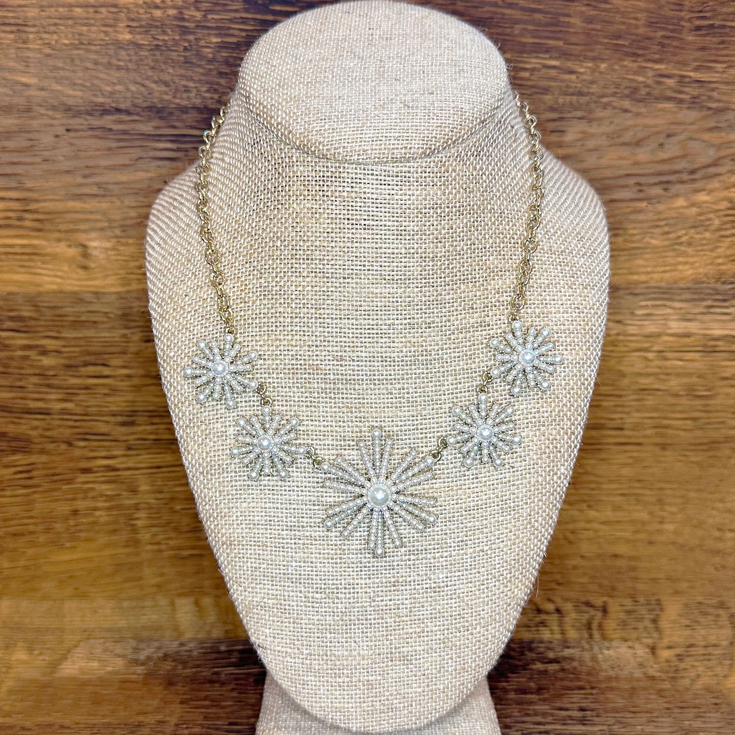 A golden necklace with a firework pattern of pearls displayed on a mannequin bust.