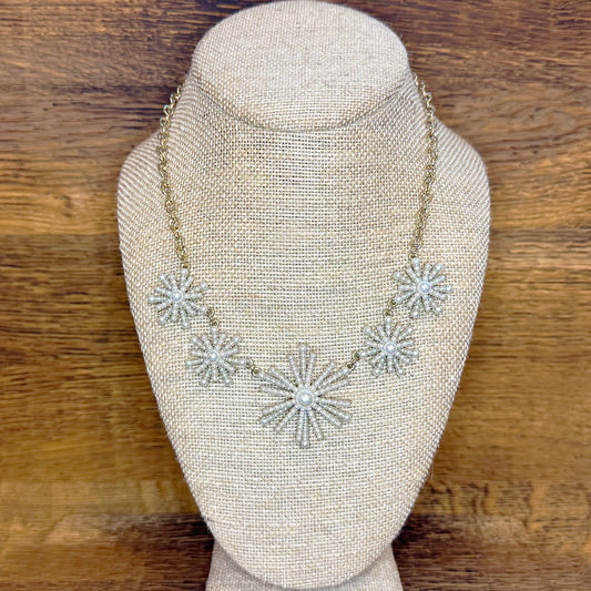 A golden necklace with a firework pattern of pearls displayed on a mannequin bust.