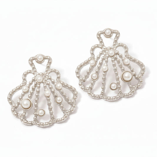 Pair of ornate shell earrings with pearls on a white surface