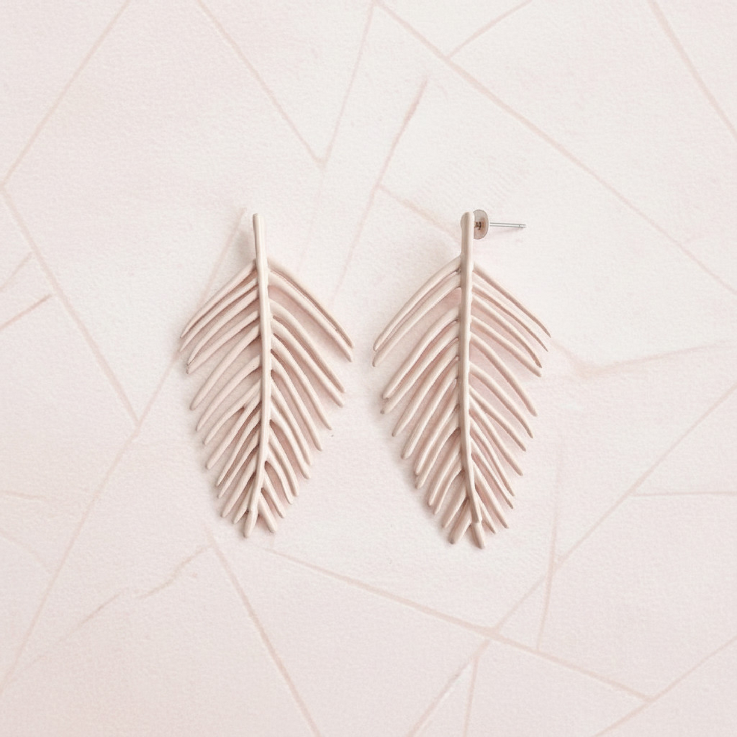 Pair of leaf-shaped earrings on a light pink geometric patterned background