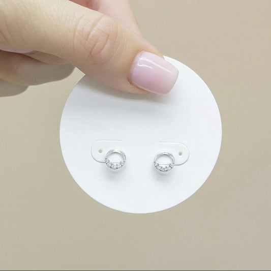 Hand holding a small round card with earrings against a neutral background