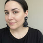 Woman wearing black raffia earrings against a neutral background