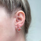 Close-up of an ear wearing red crab-shaped earrings with a light background