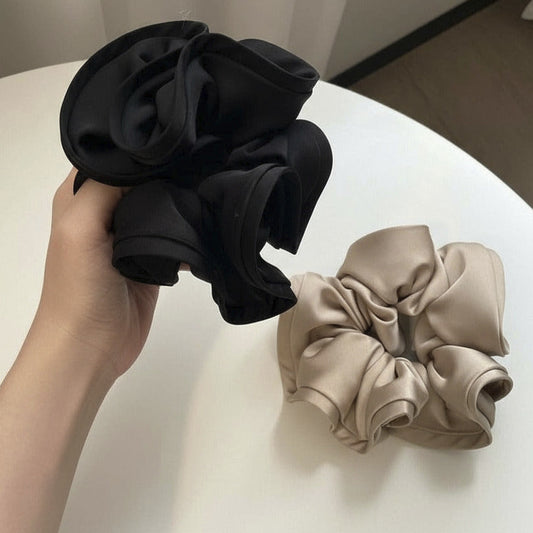 Black and beige scrunchies held by a hand on a white surface.