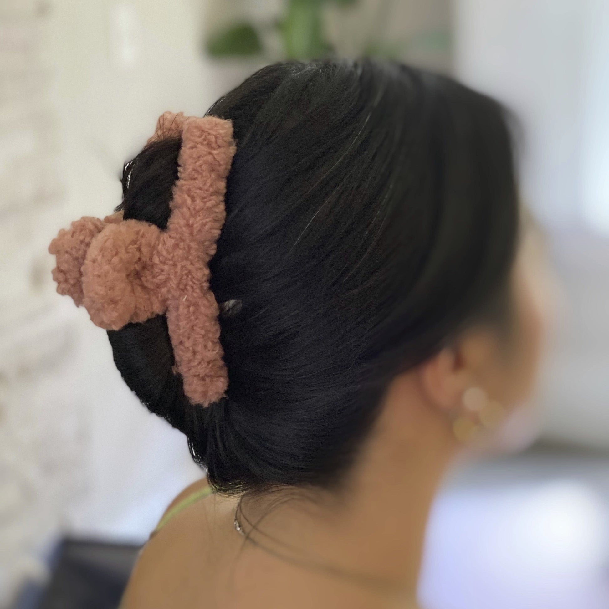 Person with a bun wearing a tan fuzzy claw clip, blurred background