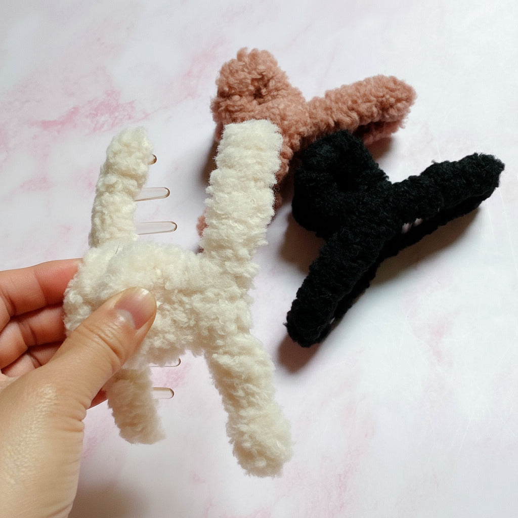 Three plush star-shaped hair clips in white, tan, and black on a light pink background.