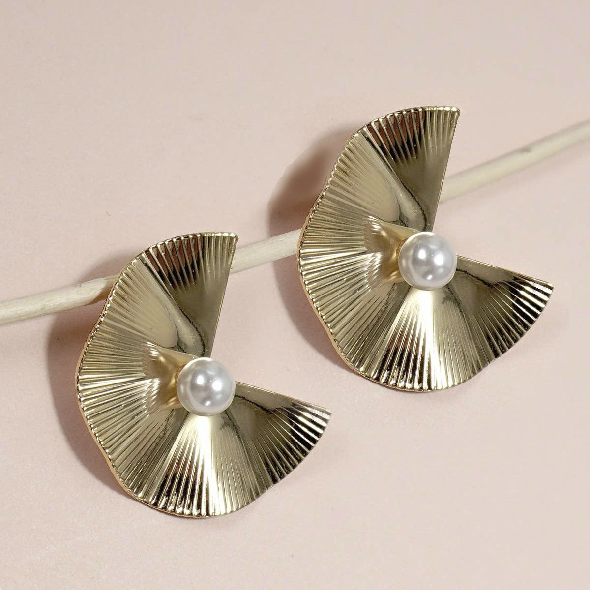 Gold earrings with pearl centers on a light pink background