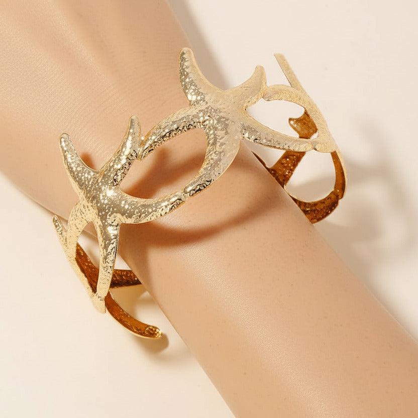 Gold starfish bracelet on an arm against a beige background