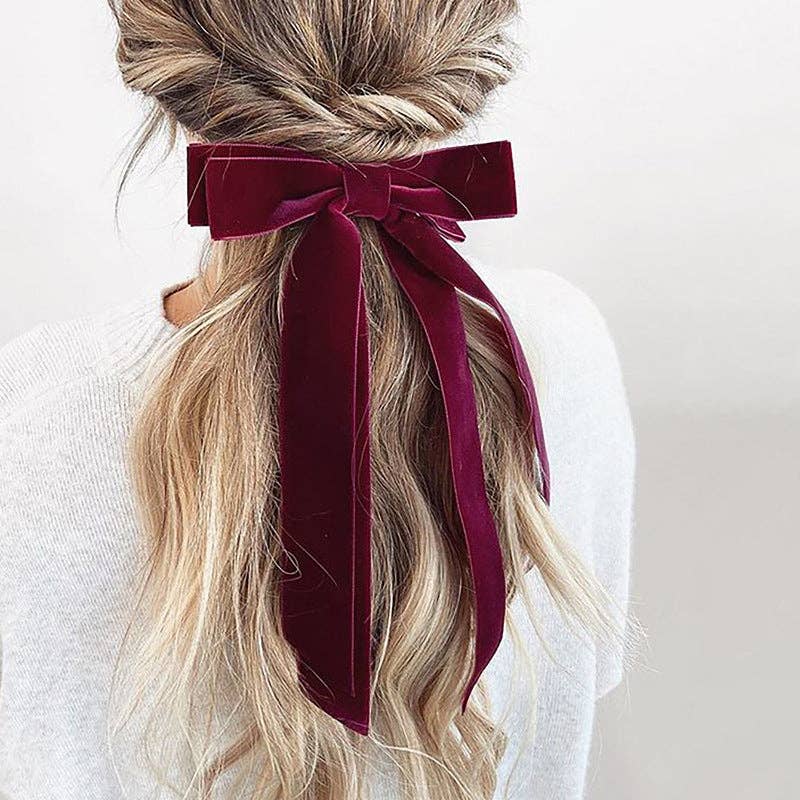Blonde hair styled in a bun with a burgundy ribbon against a light background