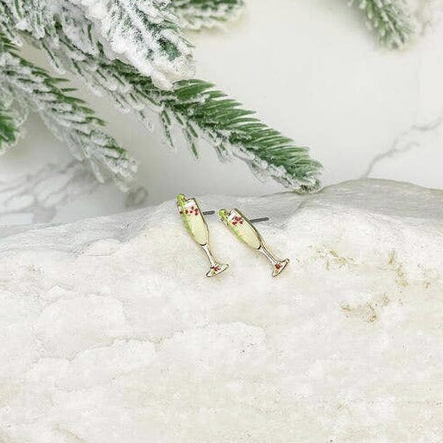 Champagne flute earrings on a white stone surface with greenery
