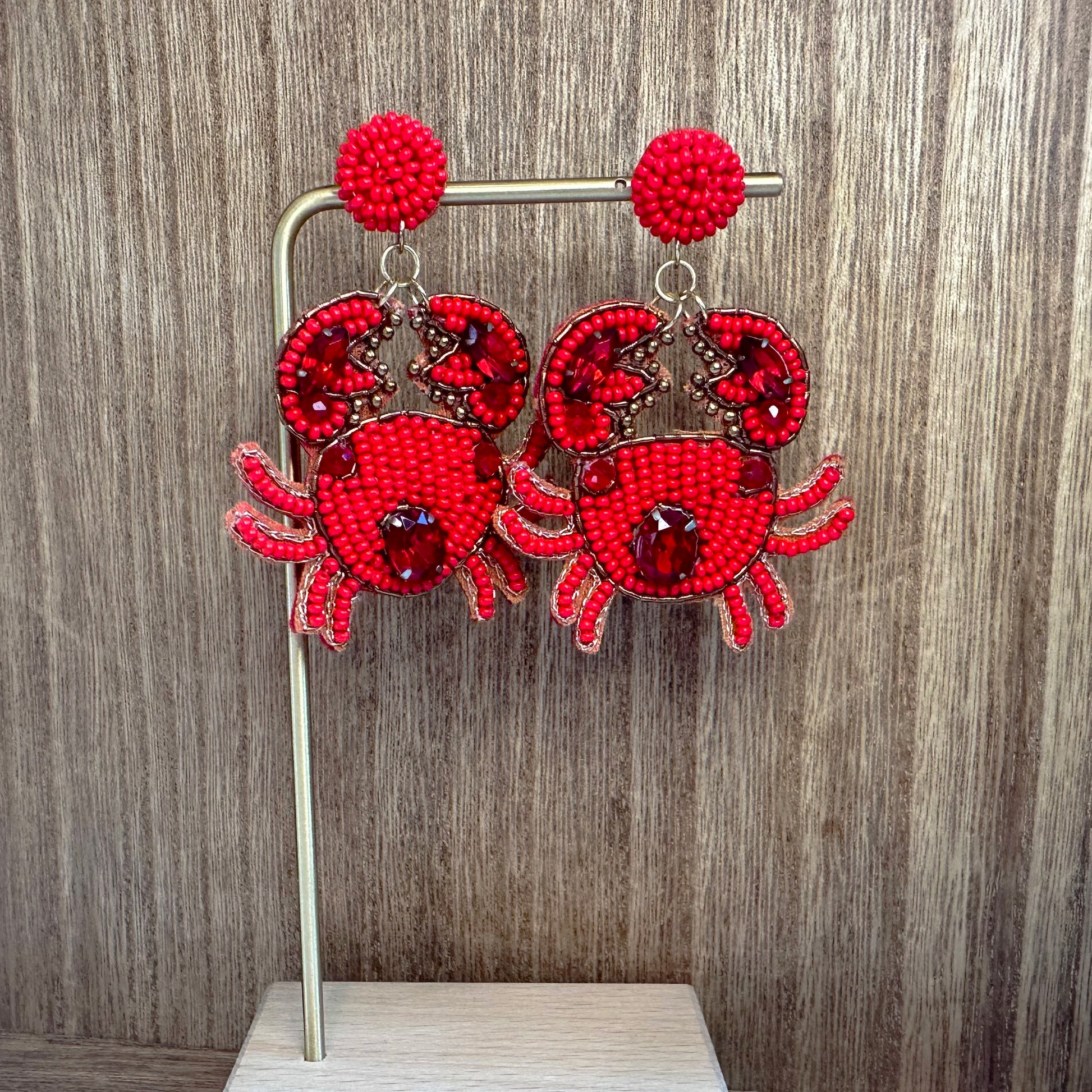 A pair of red beaded earrings designed to resemble crabs, displayed on a wooden surface.