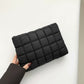 Black quilted clutch held by a hand against a neutral background