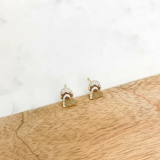 Gold dog-shaped earrings on a white card, placed on a wooden surface.