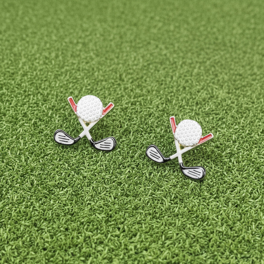 Golf club and ball earrings on a white surface with greenery in the background