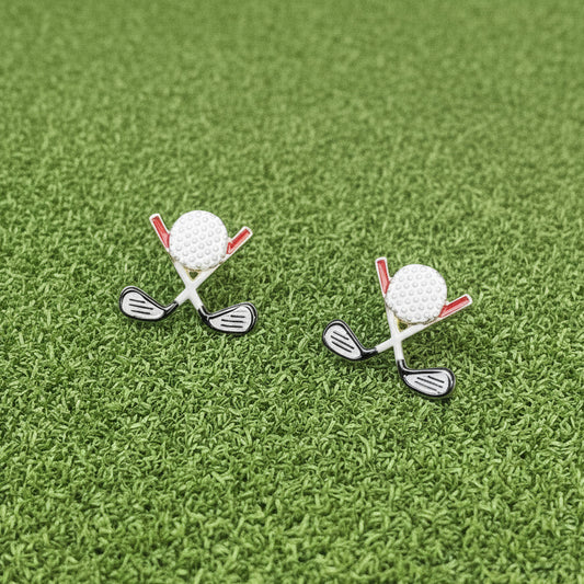 Golf club and ball earrings on a white surface with greenery in the background