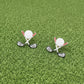 Golf club and ball earrings on a white surface with greenery in the background