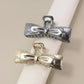 two metallic bow-shaped hair clips on white and beige background