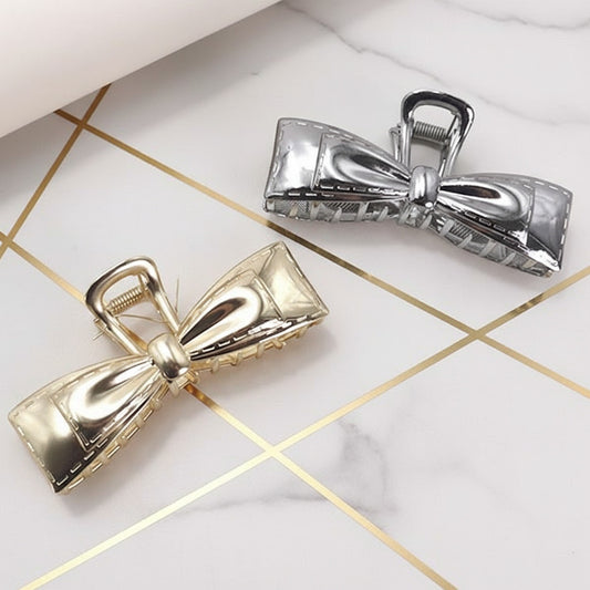 Two metallic bow-shaped hair clips on a textured background