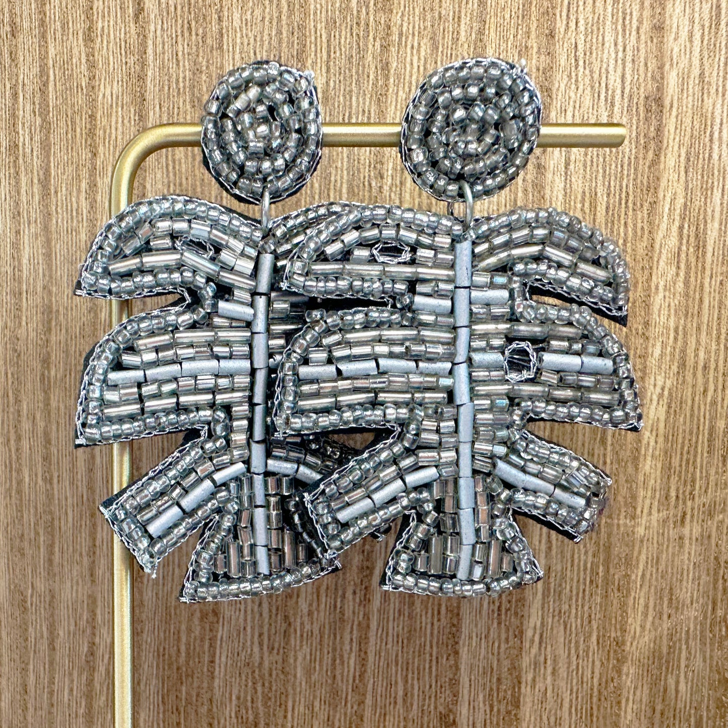 metallic beaded palm earrings in silver against a wood background
