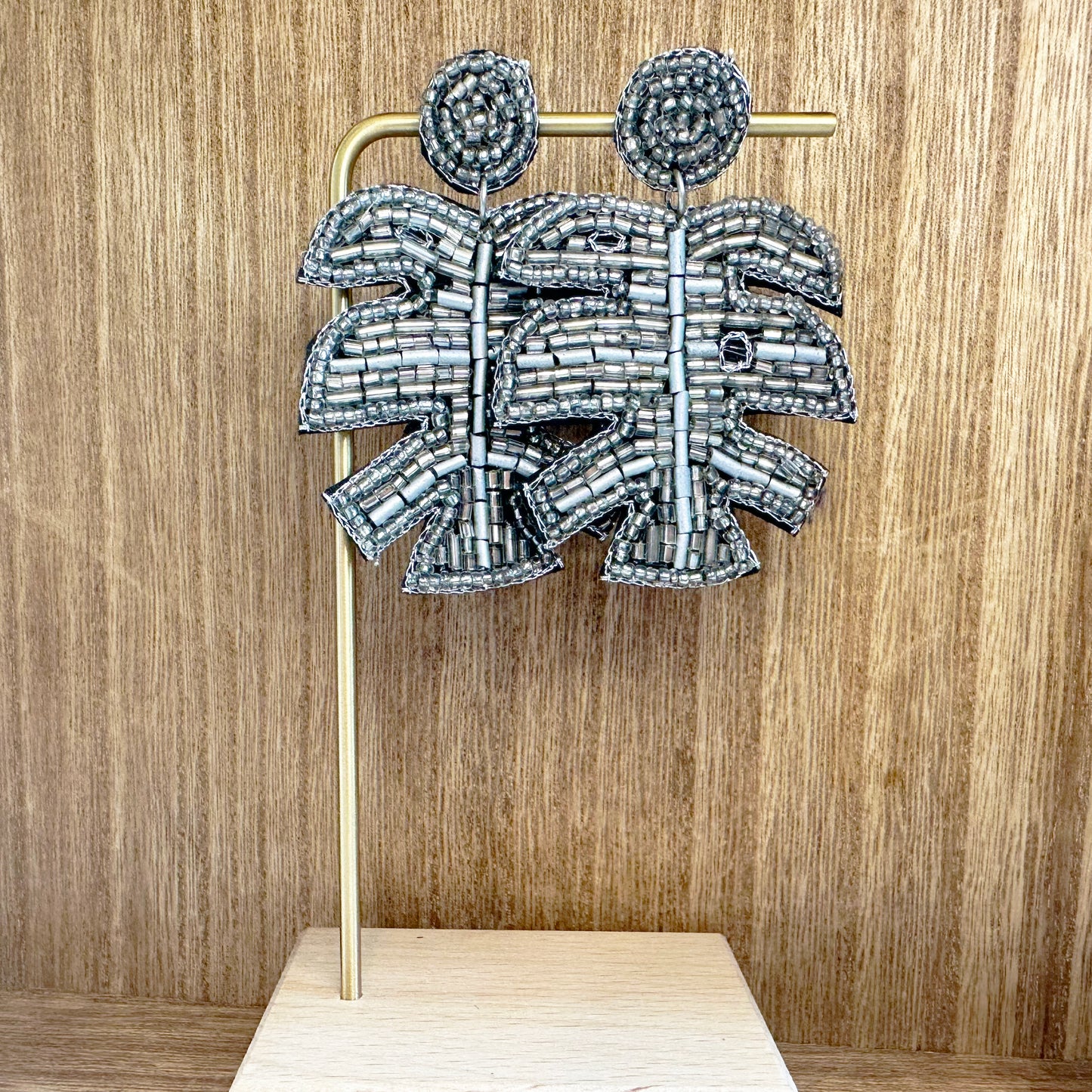 A pair of metallic silver beaded dangle palm earrings displayed on a wooden surface.
