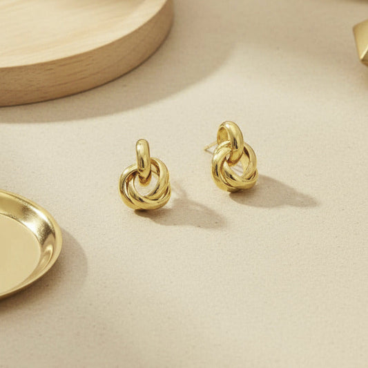 Gold knot earrings on a neutral background