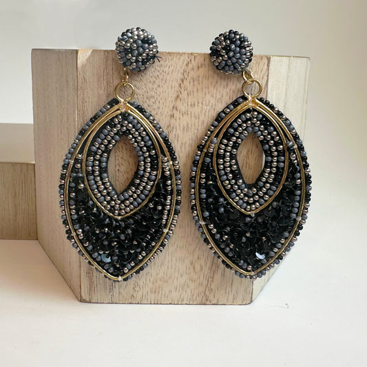 oval beaded statement earrings in black with gold accents against a wood background