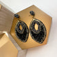 oval beaded statement earrings in black with gold against a gold riser