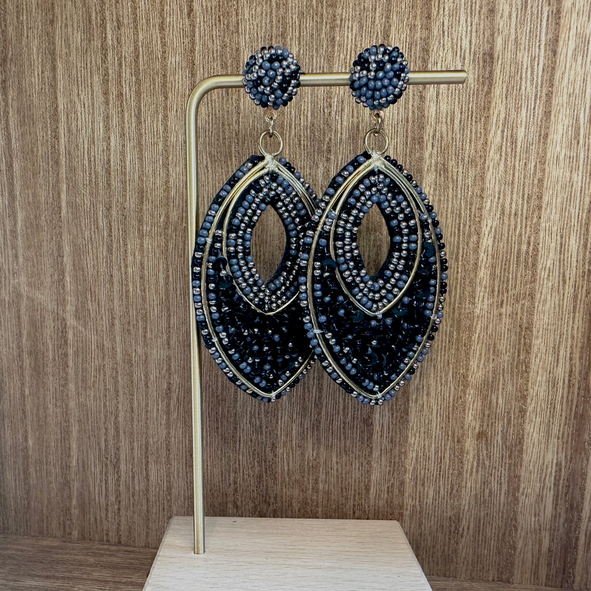 oval beaded statement earrings in black with gold accents against a wood background
