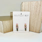 Stud earrings with pink nutcracker enamel design displayed on a card with 'Boutique 831' branding.