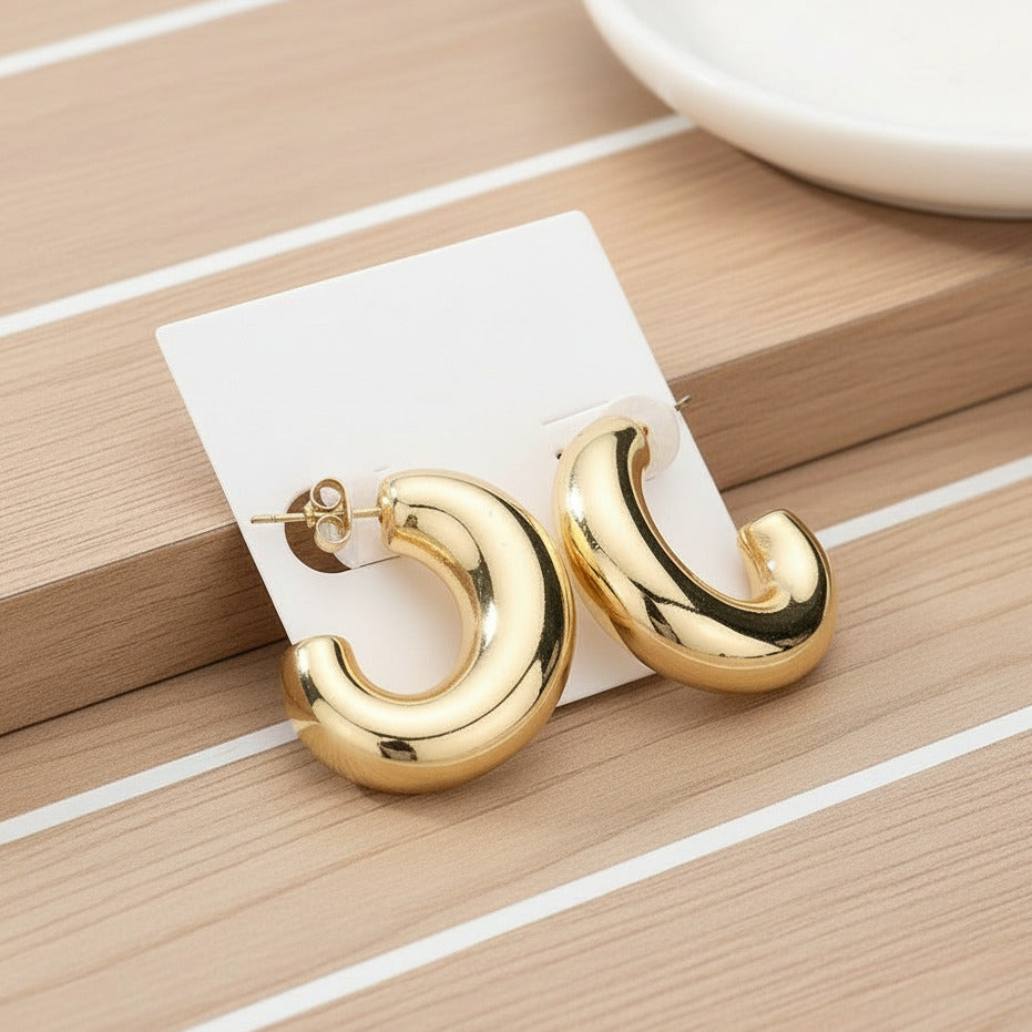 Gold dipped metal oval hoop earrings on a white card, with a striped wood background.