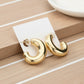 Gold dipped metal oval hoop earrings on a white card, with a striped wood background.