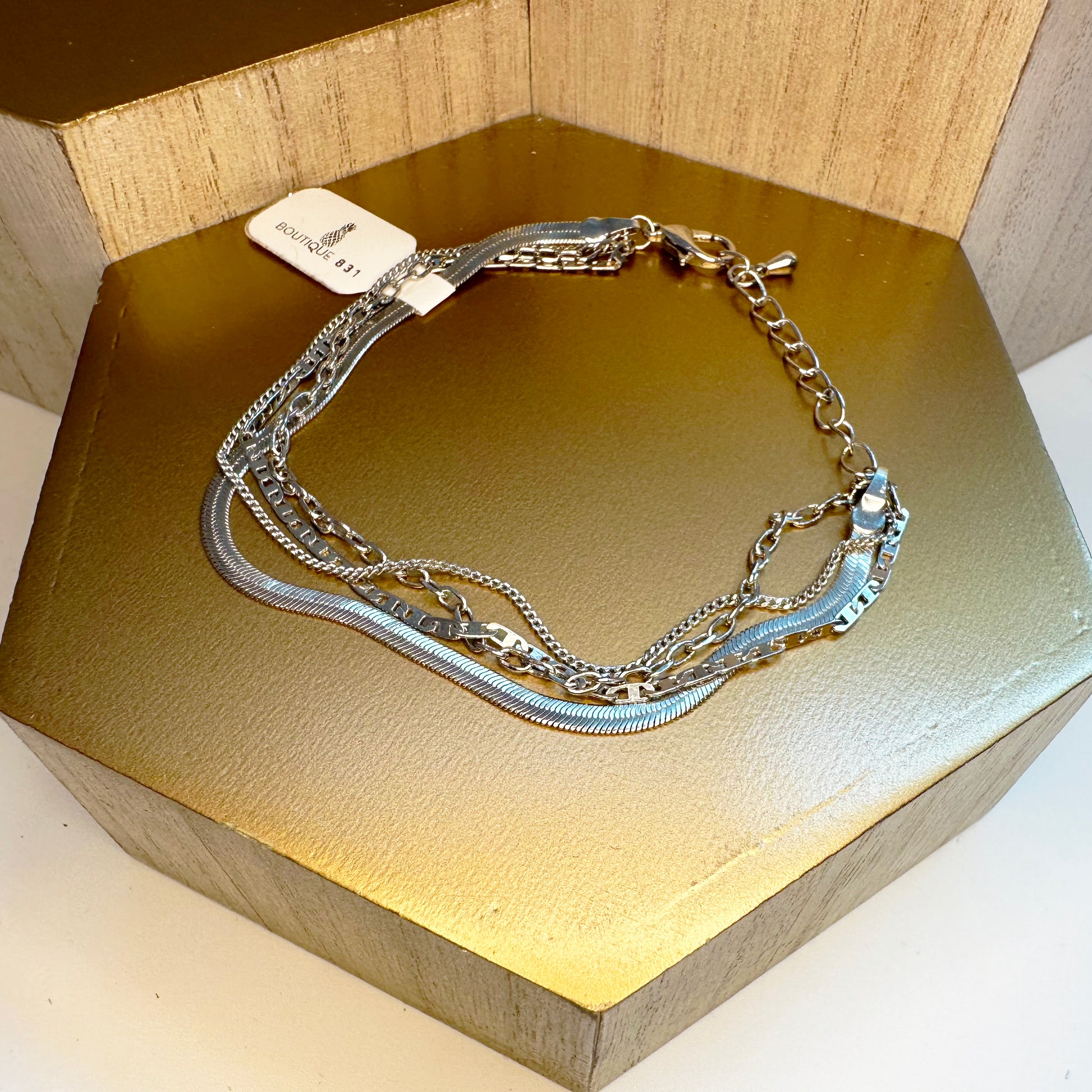 A silver multistrand bracelet with a lobster claw clasp, displayed on a gold-colored surface.