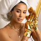Woman with gold jewelry and a towel on her head, holding gold foil gloves.