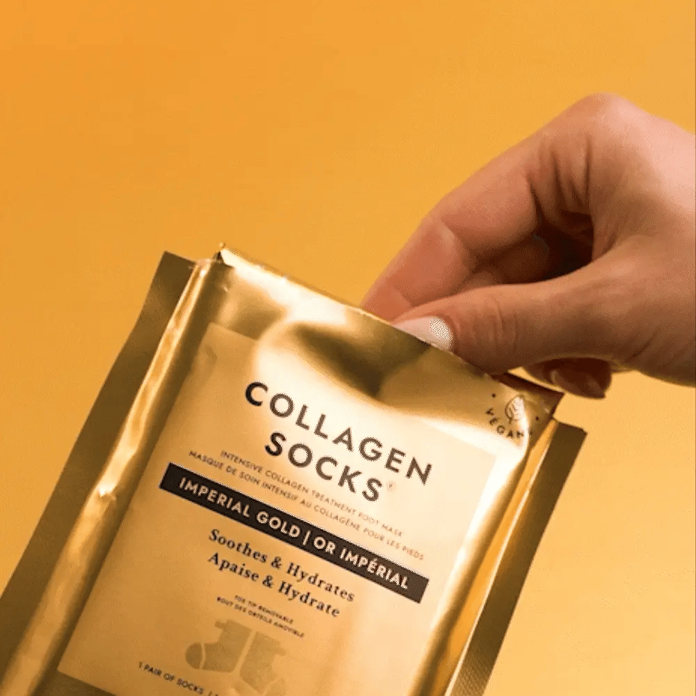 Gold packaging of Collagen Socks with a hand holding it against a yellow background