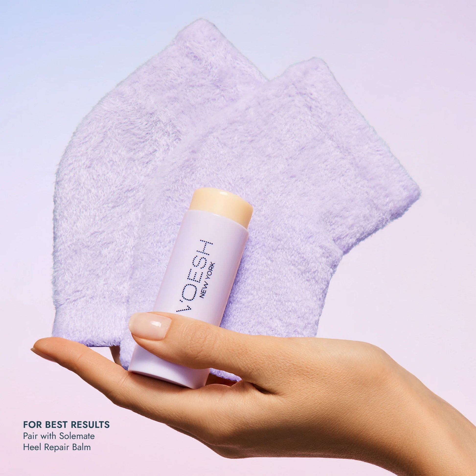 Hand holding a stick of VOESH heel repair balm with a purple towel in the background